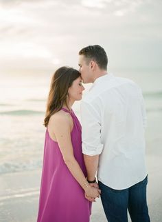 an engaged couple standing on the beach holding hands and looking into each other's eyes