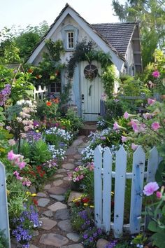 a white house surrounded by lots of flowers and greenery with a stone path leading to the front door