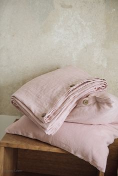 a stack of pink linens sitting on top of a wooden bench next to a wall