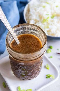 a jar filled with brown liquid sitting on top of a white plate next to rice