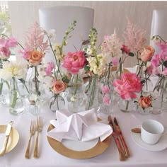 the table is set with pink and white flowers in vases, silverware, and napkins