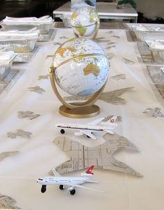 a table topped with lots of model airplanes and globes on top of paper plates