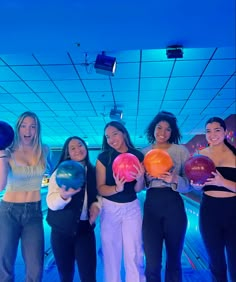 four girls are posing for the camera with their bowling balls in front of blue lights