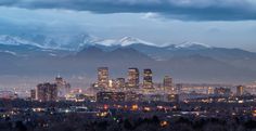 the city is lit up at night with snow capped mountains in the backgroud