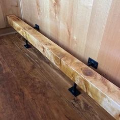 a wooden bench sitting on top of a hard wood floor next to a wall with black handles