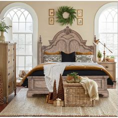 a large bed sitting in a bedroom next to two tall windows with wreaths on them