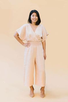 a woman standing with her hands on her hips wearing a white jumpsuit and sandals