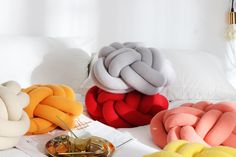 four different colored pillows sitting on top of a white bed next to a gold lamp