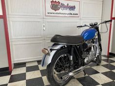 a blue and white motorcycle parked in front of a garage door on a checkered floor