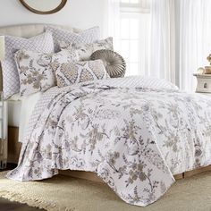 a bed with white and grey comforters in a bedroom next to a window on a rug