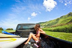 a woman sitting in the back of a pick up truck next to a surfboard