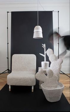 a white chair sitting next to a vase with a flower in it on top of a black mat