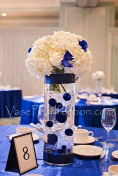 a vase with white and blue flowers is on a table set for an elegant dinner