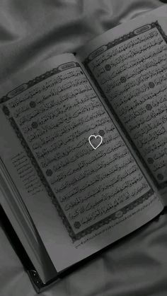 an open book with arabic writing and a heart in the middle on a satin surface