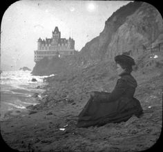 an old photo of a woman sitting on the edge of a cliff by the ocean