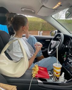 a woman sitting in the driver's seat of a car eating food and drinking