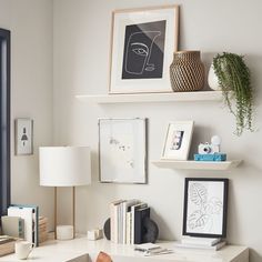 a white desk topped with lots of books next to a lamp and pictures on the wall