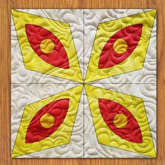 four square quilts with red and yellow designs on them sitting on a wooden surface