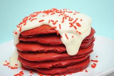 a stack of red velvet pancakes with white icing and sprinkles