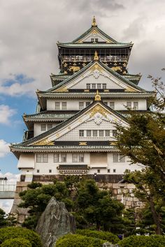 a tall white and gold building sitting on top of a lush green forest covered hillside