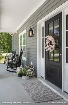 a porch with rocking chairs and flowers on the front door, in front of a gray house