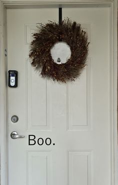 a white door with a brown wreath on it and the word boo written in black