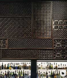 an assortment of liquor bottles on shelves in a bar with decorative wooden screens behind them