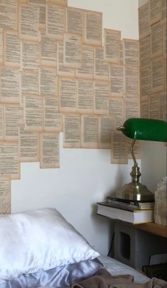 a bed sitting under a green lamp next to a wall covered in old book pages