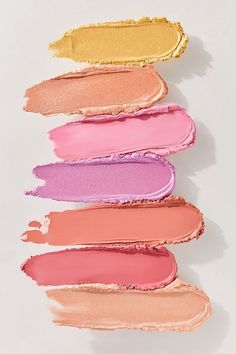 five different shades of lipstick lined up on a white surface, with one pink and one yellow