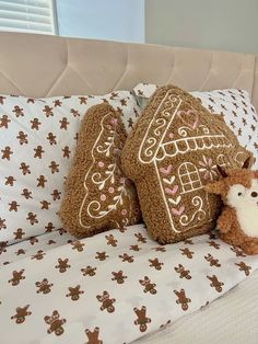 a teddy bear is laying on a bed with two gingerbread house pillows and a stuffed animal