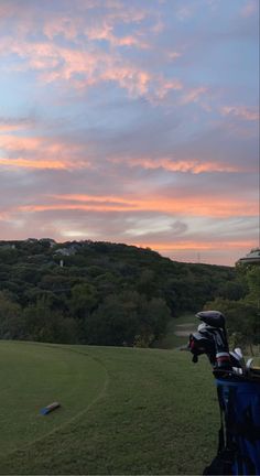 a person on a golf course with the sun setting in the background and clouds above