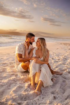 a man and woman are sitting on the beach at sunset, looking into each other's eyes