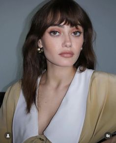 a woman with brown hair and blue eyes wearing a white top is looking at the camera