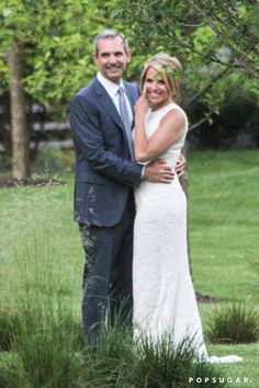 a man and woman standing next to each other in front of a tree with their arms around each other