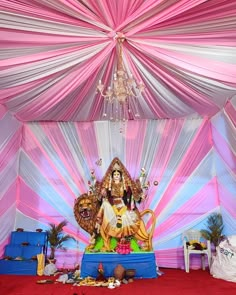 an idol sitting on top of a blue platform under a pink and white drape