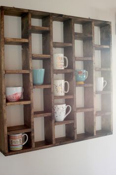 a wooden shelf filled with cups and mugs on top of a white wall next to a mirror