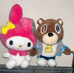 two stuffed animals sitting next to each other on top of a shelf in front of a white wall