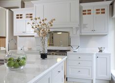 a large kitchen with white cabinets and marble counter tops, along with green apples in a bowl on the island