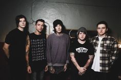 five young men standing in front of a wall with tattoos on their arms and shoulders