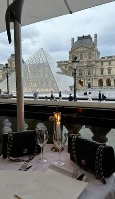 the table is set with two glasses and place settings for an event in front of a glass pyramid