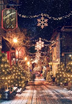 a snowy street with christmas lights and snowflakes hanging from the buildings on both sides