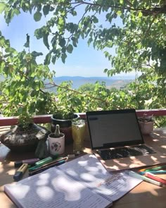 an open laptop computer sitting on top of a wooden table next to a book and pencils