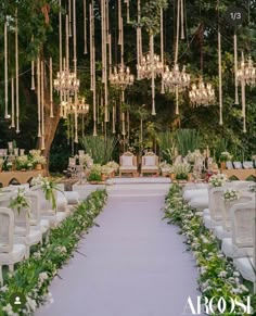 an outdoor wedding setup with white chairs and chandeliers hanging from the ceiling, surrounded by greenery