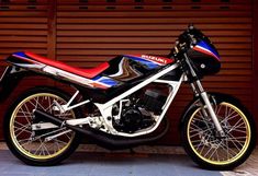 a red, white and blue motorcycle parked in front of a garage door with shutters