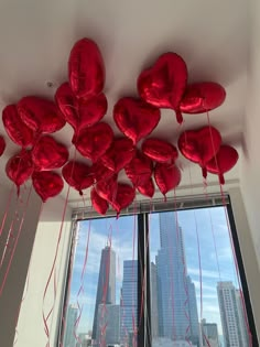 red heart shaped balloons hanging from the ceiling in front of a window with skyscrapers