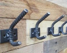 three metal hooks are attached to the side of a wooden wall with two black hoses