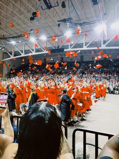 graduates in orange graduation gowns toss their caps into the air as they walk through an arena