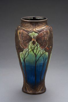 a vase with a butterfly painted on the side and trees in the middle, against a gray background