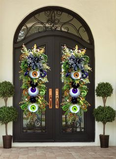 two decorated halloween wreaths on the front door of a house with potted plants