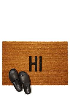 a pair of slippers sitting next to a door mat with the word h on it